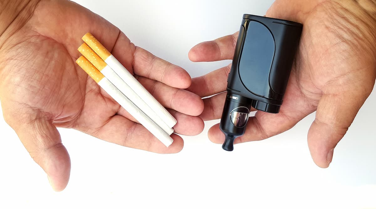 Vaping device and cigarettes in the man's hand, concept of choosing the type of cigarette