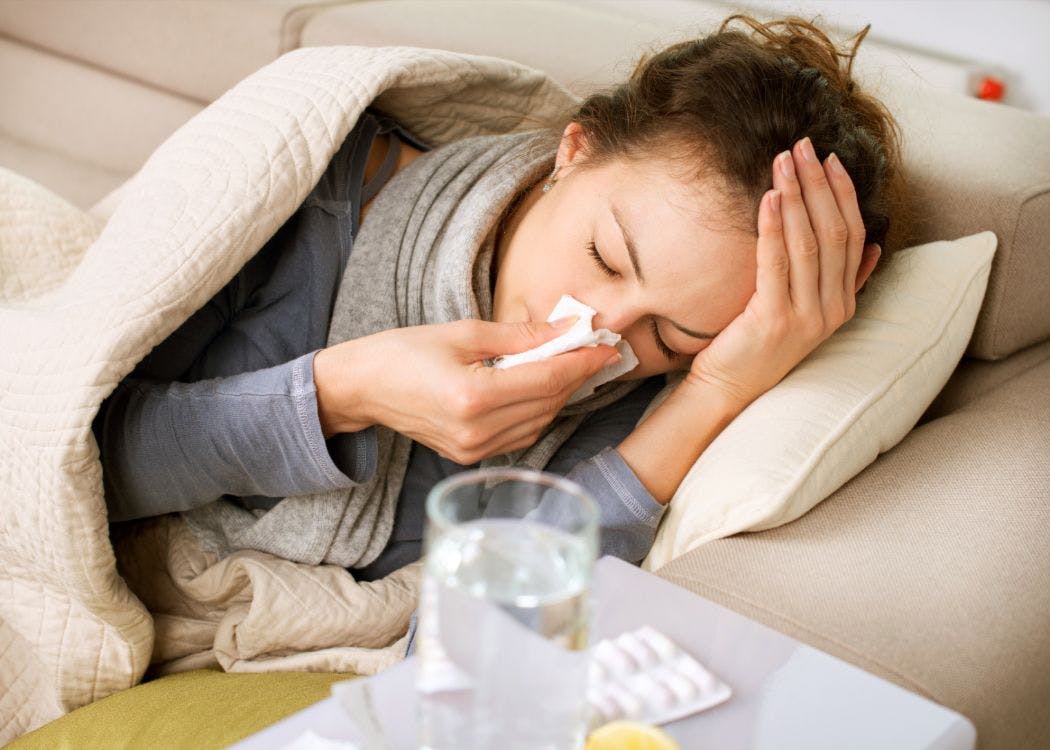 woman blowing her nose and holding her head while sick, woman sick with the flu